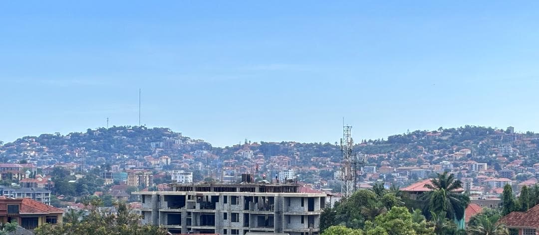 Unfinished concrete frame below a densely built hillside, with a telecom mast and blue sky