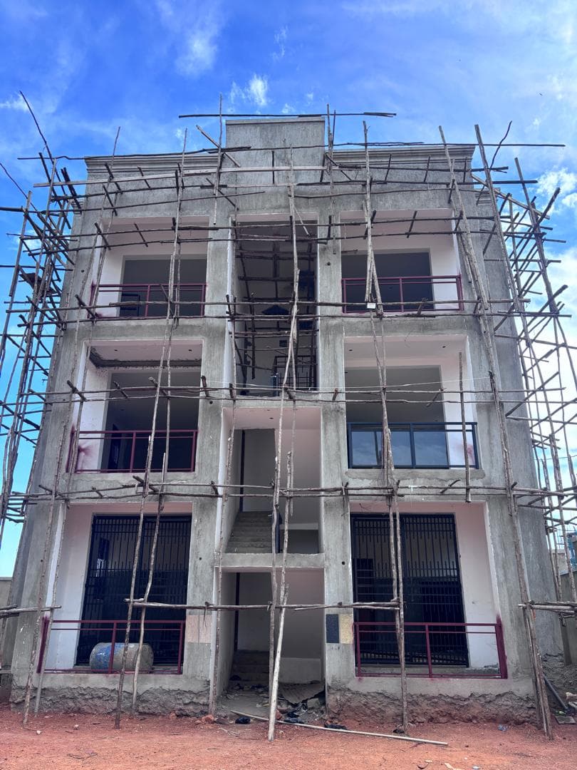 Straight-on view of an unfinished concrete apartment facade with pink balcony rails and scaffolding