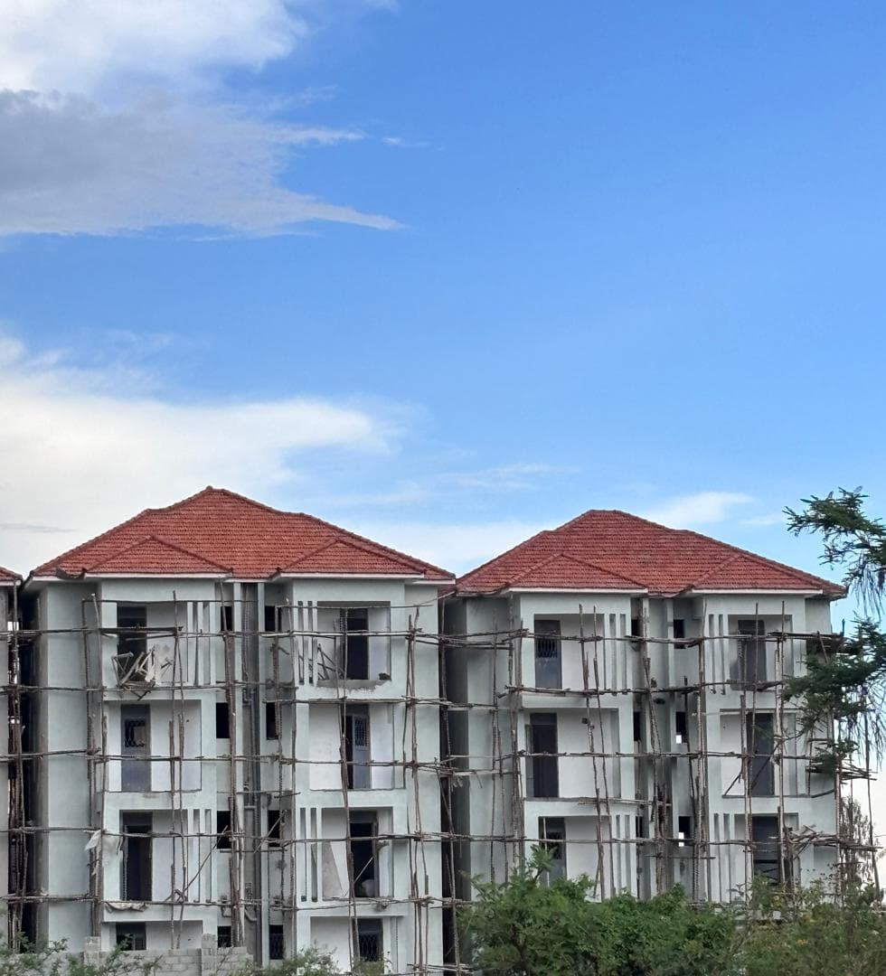 White residential buildings with red tiled roofs, balconies and scaffolding beneath a blue sky